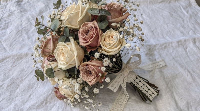 Getrockneter Hochzeitsstrauß aus cremefarbenen Rosen auf weißem Leinen