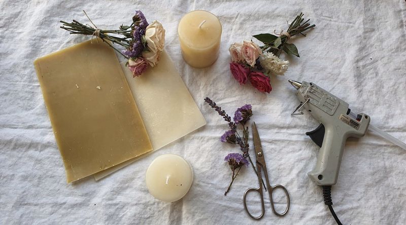 Materialflatlay: Wachsplatten in verschiedenen Farben, Trockenblumen, Kerzen und Werkzeuge auf Leinentuch