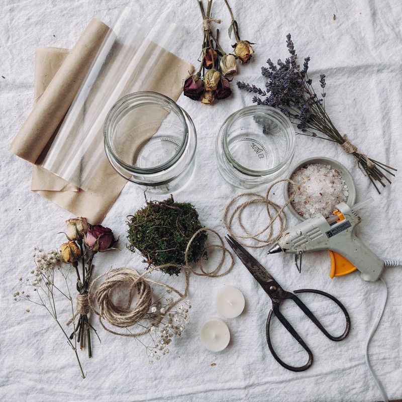 Materialflatlay: Gläser, Papier, Trockenblumen, Moos und Naturschnüre übersichtlich arrangiert auf Leinentuch