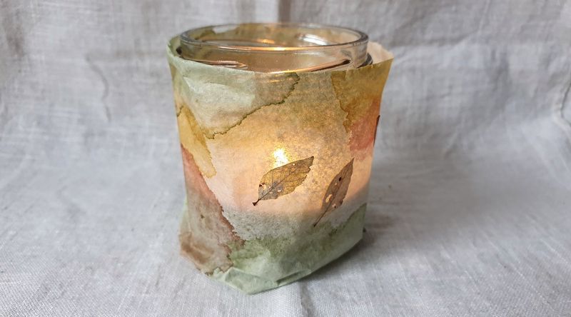 Fertiges Aquarell-Windlicht mit sanften Grün- und Goldtönen, leuchtend von innen