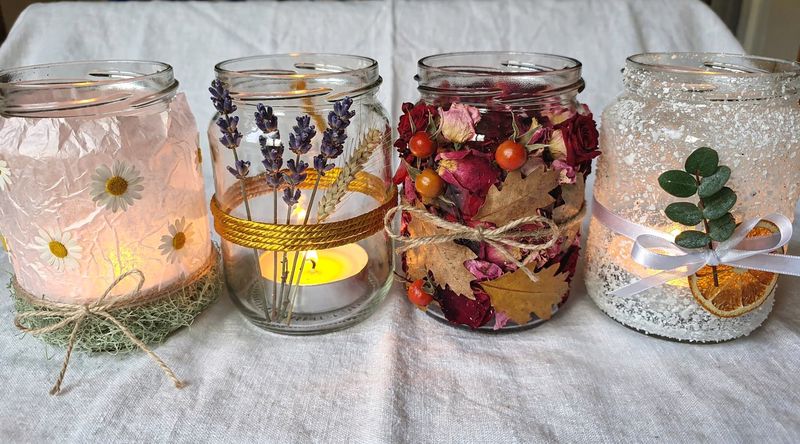 Vier Windlichter nebeneinander, jedes in einer Jahreszeit dekoriert