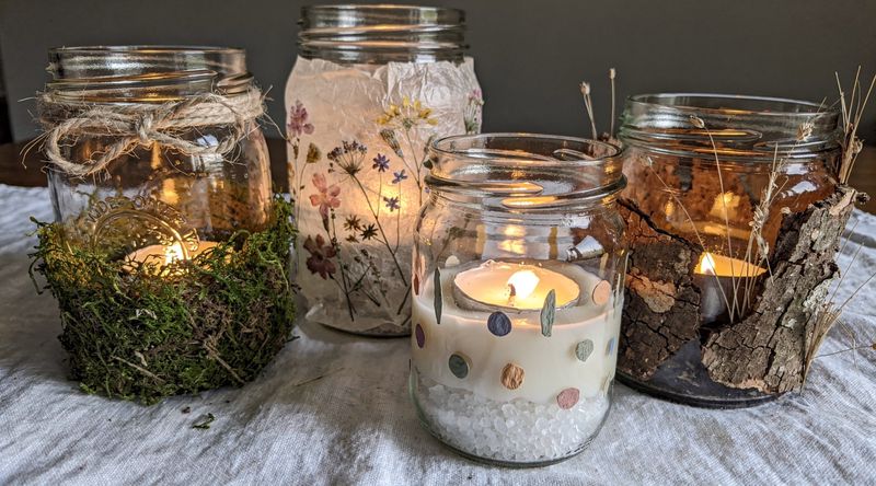 Upcycling-Windlichter aus verschiedenen alten Gläsern, jedes mit anderen Naturmaterialien verziert